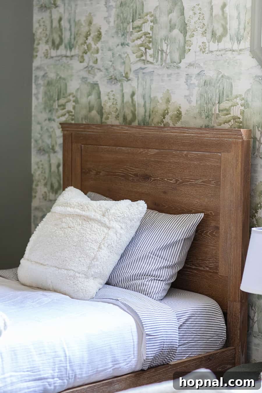 Wooden bed with soft, striped bedding from Pottery Barn, beautifully complementing the woodsy wallpaper in a kids' cabin room.
