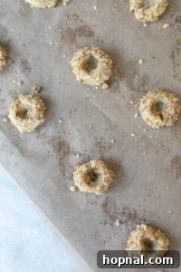 Unbaked thumbprint cookies, rolled in walnuts, with visible indentations, arranged on a baking sheet lined with parchment paper, ready for their first bake.