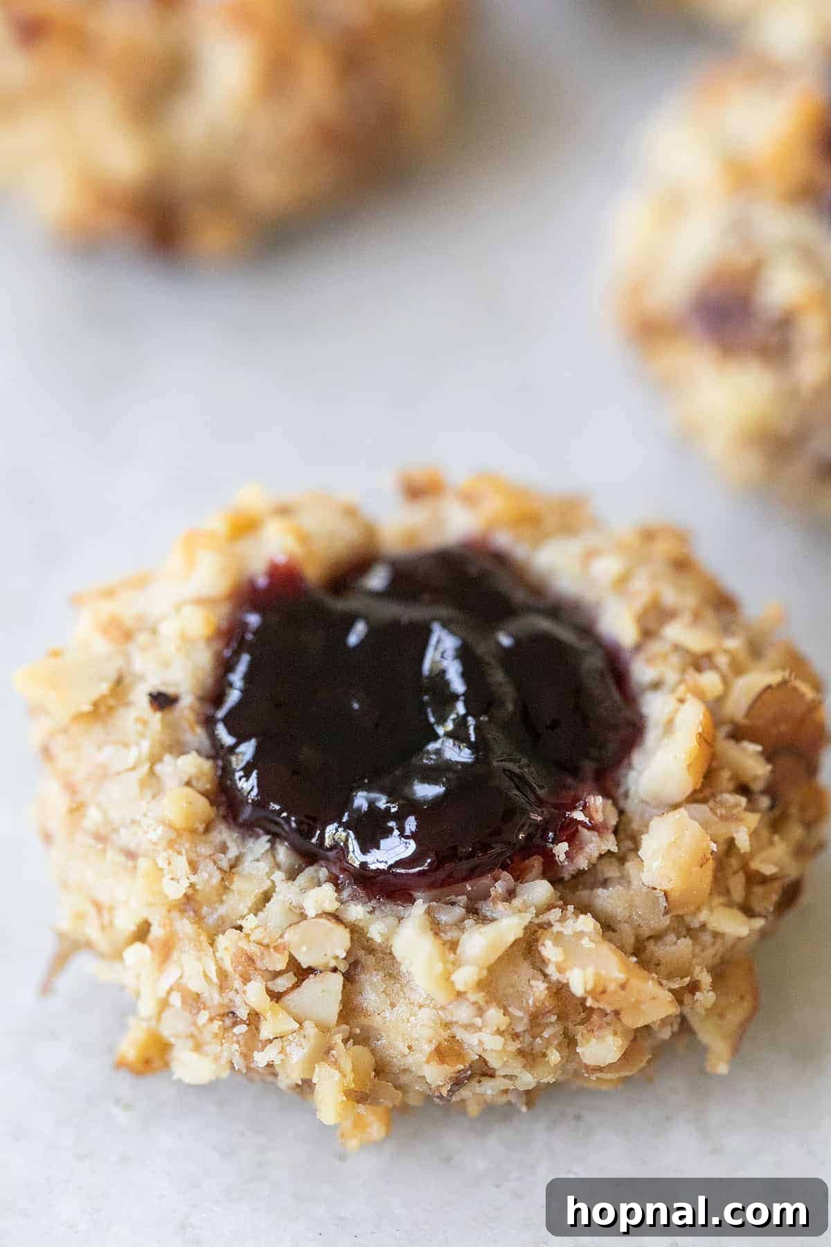 A perfectly baked Thumbprint cookie, filled with glistening raspberry jam, showcasing its golden walnut crust and irresistible appeal.