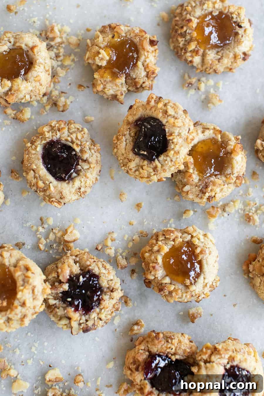A beautifully composed shot of multiple jam thumbprint cookies, each perfectly baked with a golden edge, walnut crust, and a dollop of glistening jam, highlighting the appeal of this classic recipe.