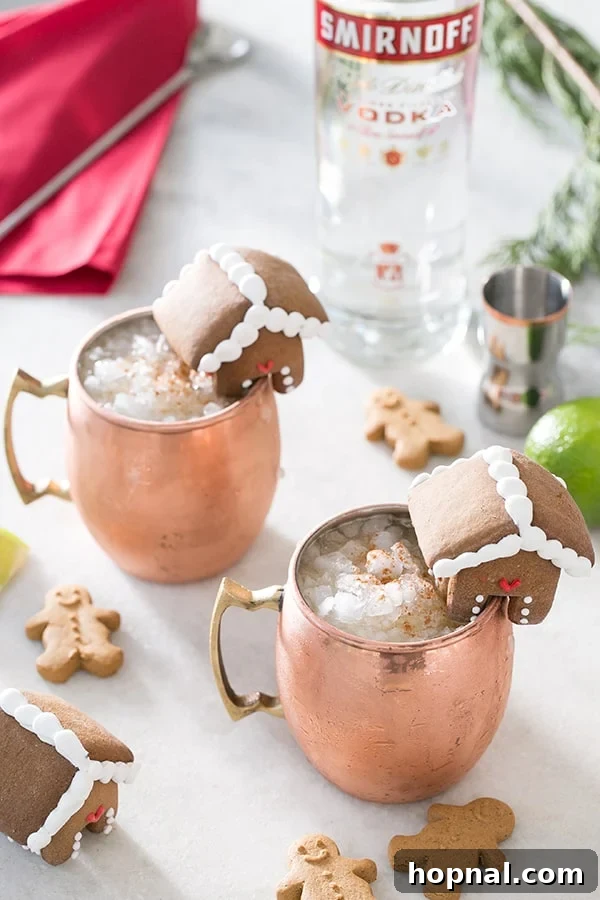 Festive Gingerbread Moscow Mule served in a copper mug with a mini gingerbread house garnish.