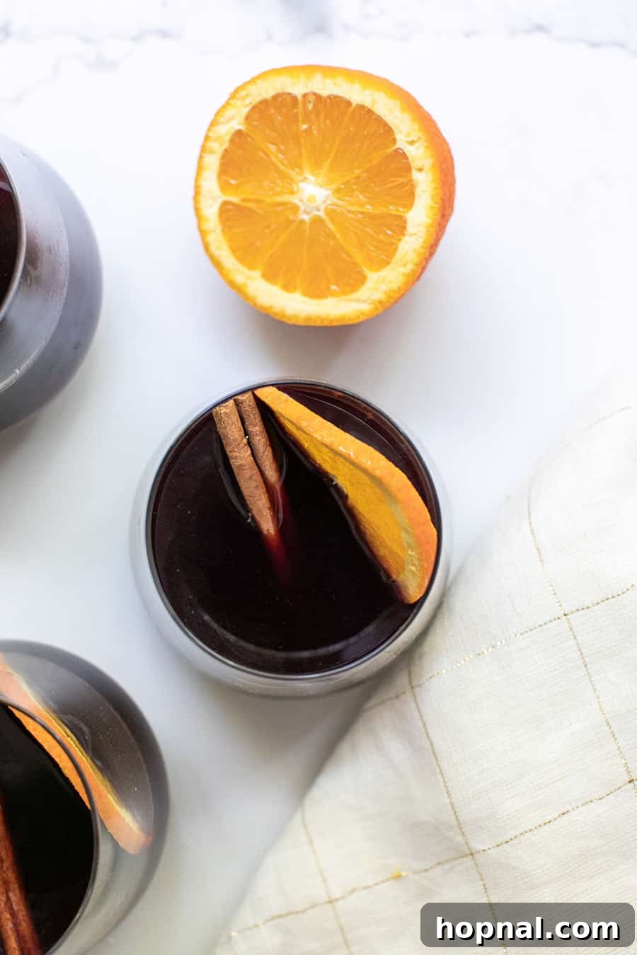 Warm mulled wine in a glass mug, garnished with an orange slice and cinnamon stick.