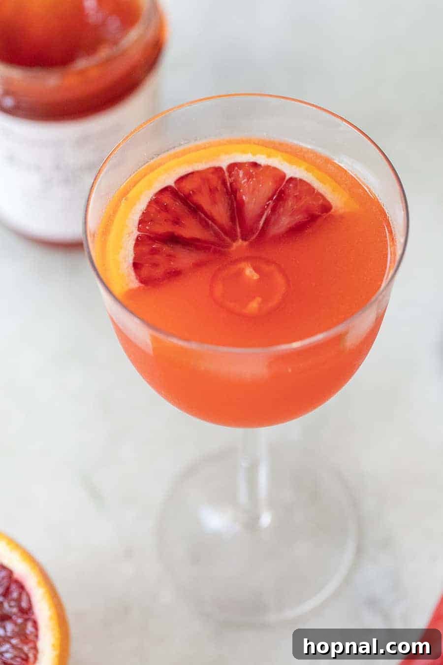Unique Red Pepper Jelly Cocktail with blood orange slice and fresh herbs.