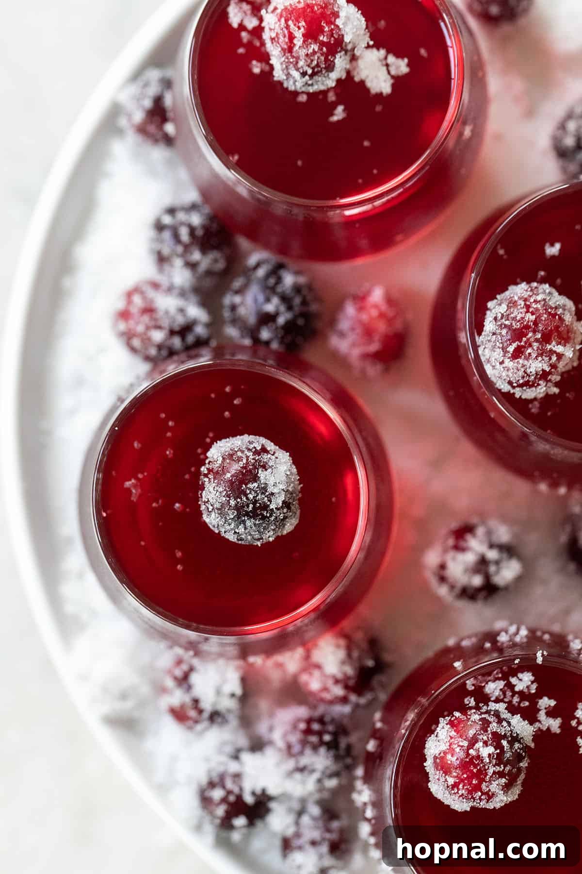 Festive cranberry jello shots in small glass shot glasses with gold spoons.