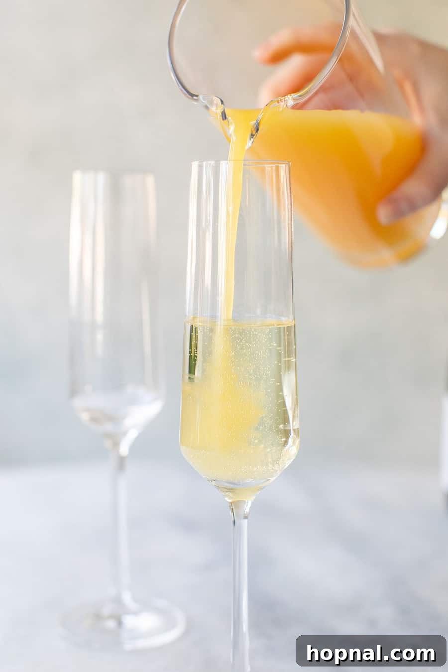 Pouring orange juice into sparkling wine in a Champagne flute, highlighting the blending process.