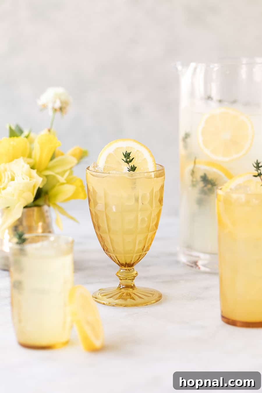 Tequila spiked lemonade with a sprig of thyme garnish in a glass with ice.