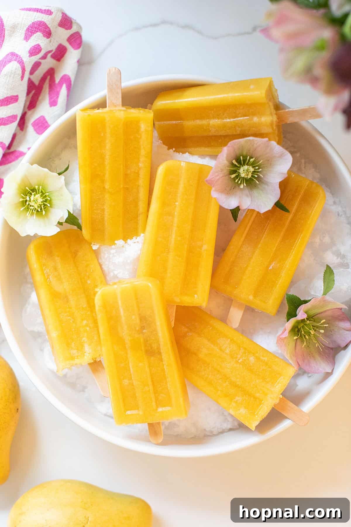 Vibrant mango popsicles arranged on a platter of ice, garnished with fresh tropical fruits like mango slices and papaya chunks, evoking a refreshing summer scene.