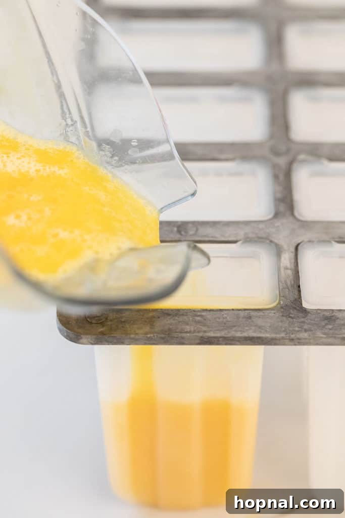 Pouring the vibrant mango and papaya juice mixture into individual popsicle molds, ensuring each mold is evenly filled for consistent popsicles.
