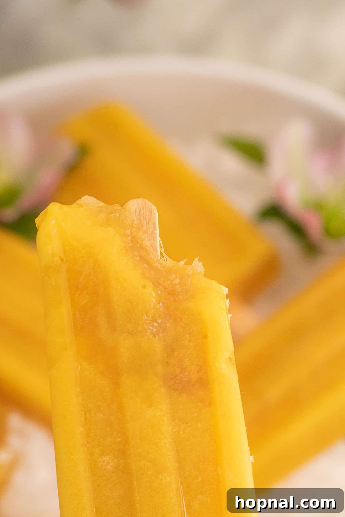A close-up shot of a mango popsicle with a bite taken out, revealing its smooth, icy texture and vibrant yellow color, emphasizing its refreshing appeal.