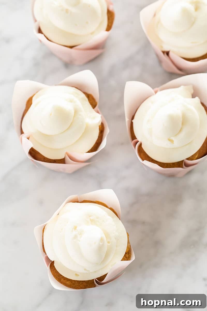 Old-fashioned carrot cake cupcakes beautifully presented in charming pink wrappers, topped with cream cheese frosting.