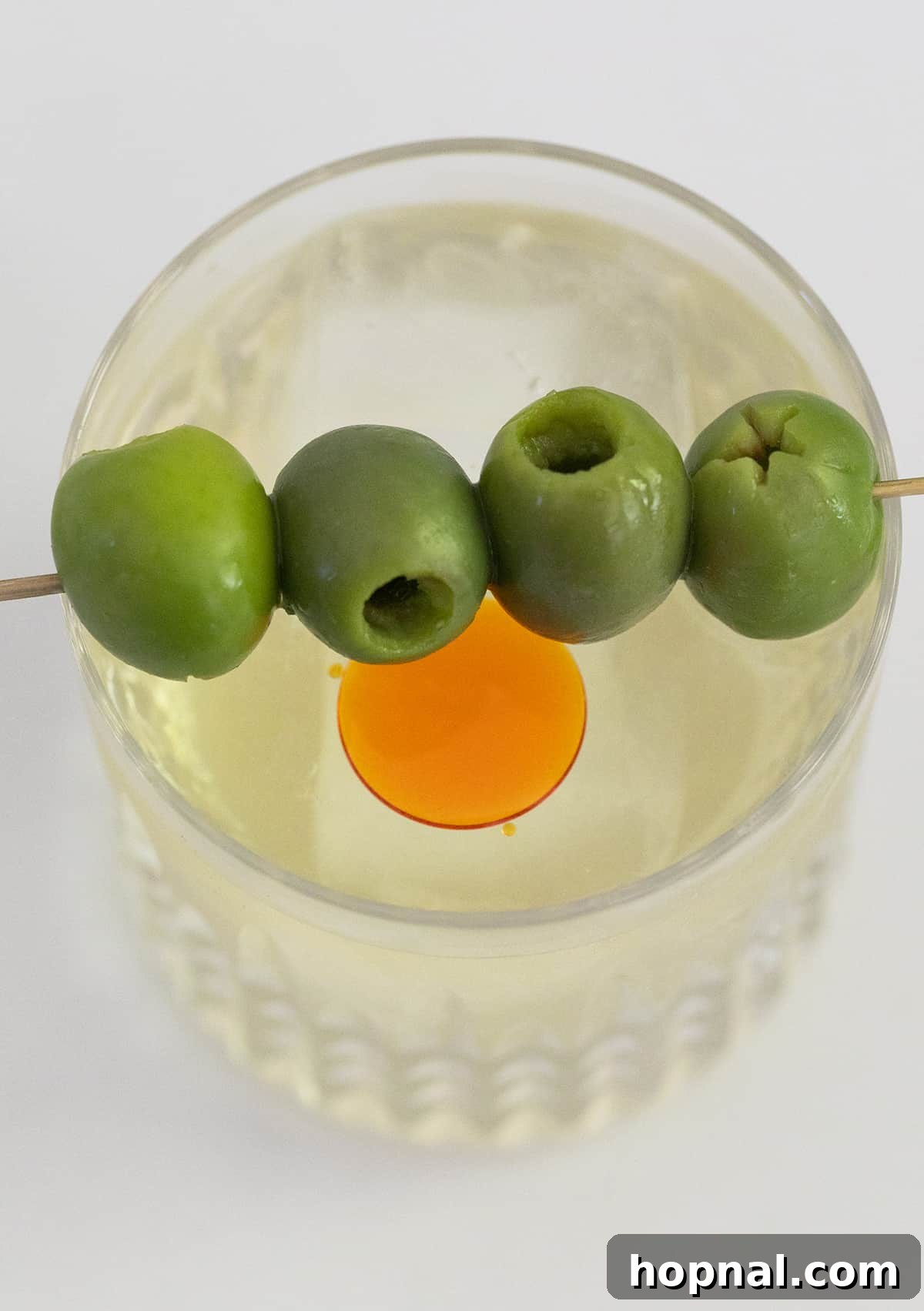 Tequila's Dirty Martini 5 A close-up photograph showcasing three vibrant green olives, perfectly pitted and skewered on a cocktail pick, poised to elegantly garnish a Dirty Martini. The focus is sharp on the smooth, glossy surface of the olives.