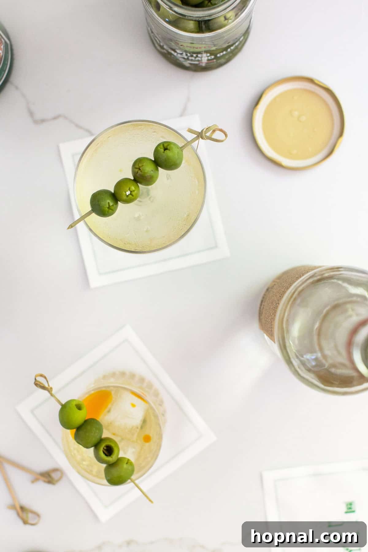 Tequila's Dirty Martini 6 A striking side-by-side photograph comparing a classic, crystal-clear Dirty Martini with our unique Tequila Dirty Martini, which features a subtle red chili oil swirl, highlighting the distinct visual differences between the two cocktails.
