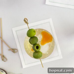 Tequila's Dirty Martini 7 A close-up shot of a Tequila Dirty Martini in a rounded, stemmed glass, elegantly garnished with two green olives and a hint of red chili oil on the surface, showcasing its unique and inviting appeal.
