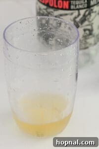 Tequila's Dirty Martini 8 The initial step of mixing a Tequila Dirty Martini: a hand carefully adds clear Blanco tequila and opaque olive brine to a cocktail shaker filled with ice, illustrating the beginning of the cocktail creation process.