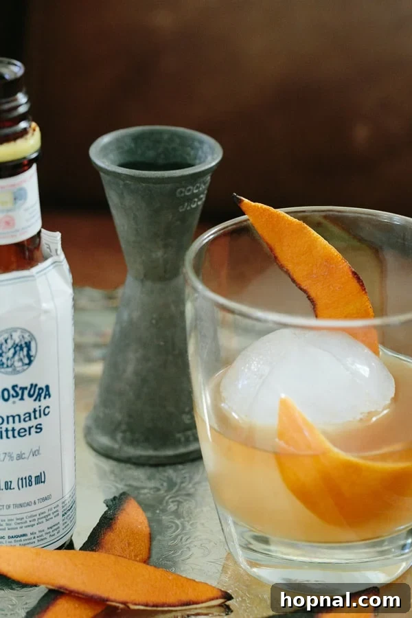 Old Fashioned cocktail recipe in a glass, garnished with burnt orange peel