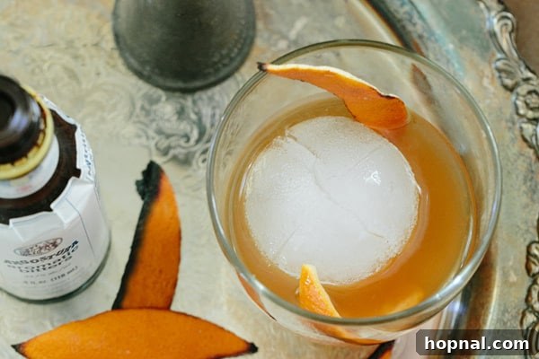 Overhead shot of a finished Burnt Orange Old Fashioned cocktail with a large ice cube and burnt orange garnish