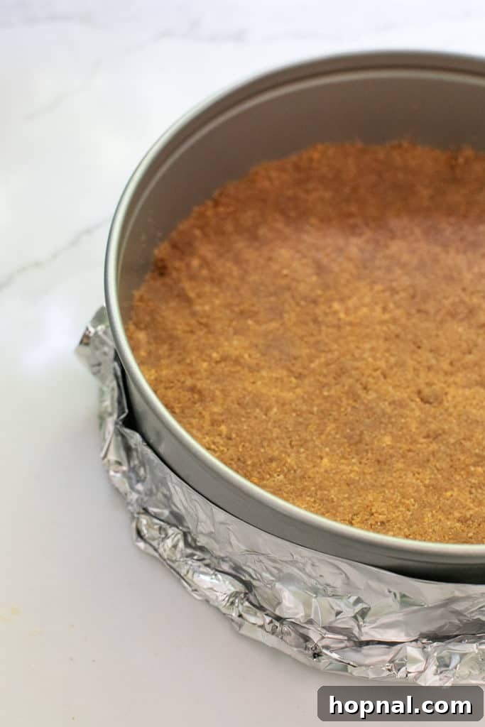 Irresistible Homemade Cheesecake 5 A perfectly pressed buttery Graham Cracker crust sits in a springform pan, wrapped in tin foil for a water bath, ready for baking.