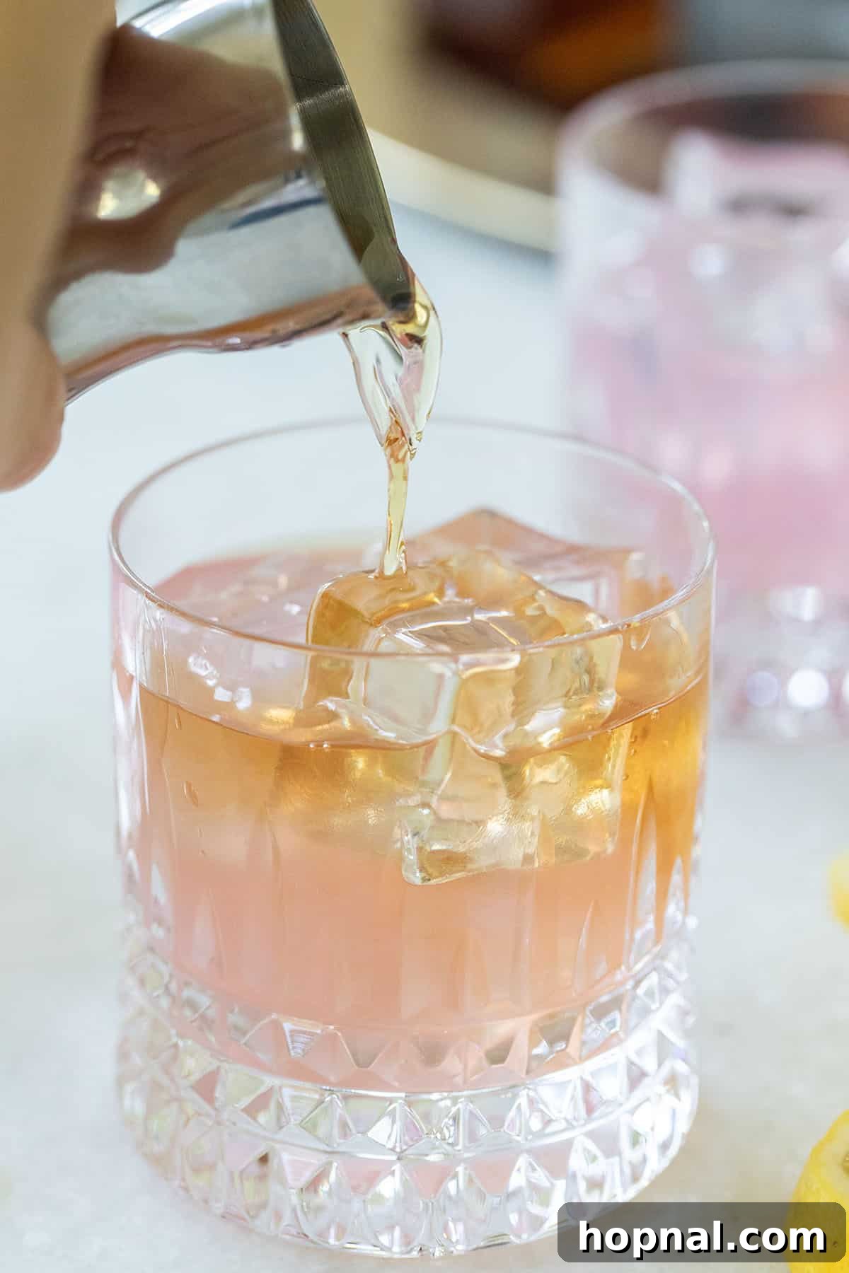 A brown spirit (whiskey) being poured over ice cubes into a cocktail glass.