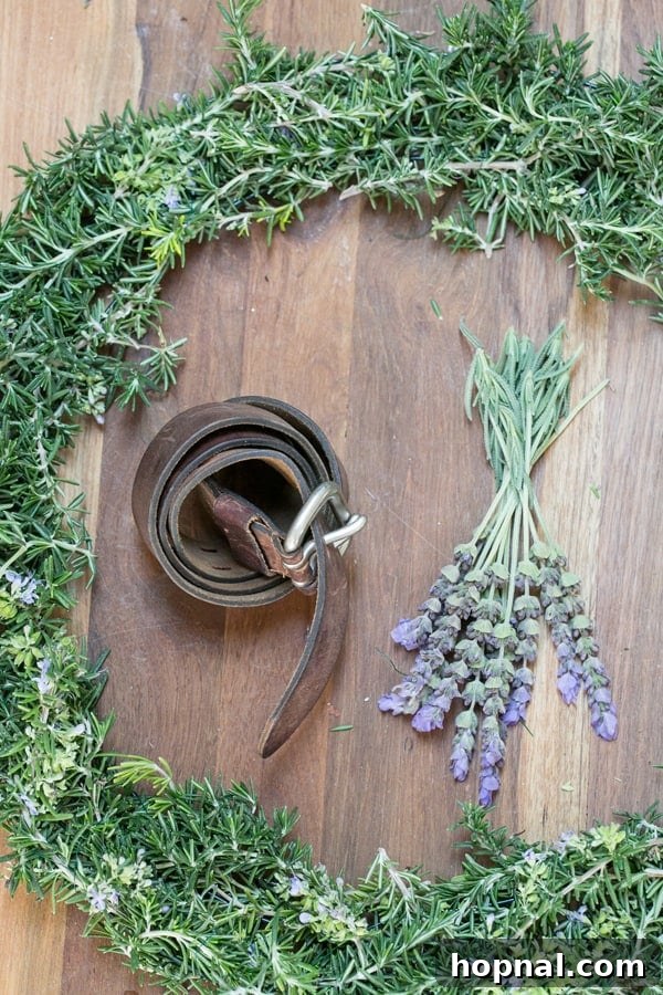 A flat lay shot showcasing all the essential materials for making a rustic rosemary wreath: fresh rosemary sprigs, a metal wreath frame, green floral wire, and needle-nose pliers.