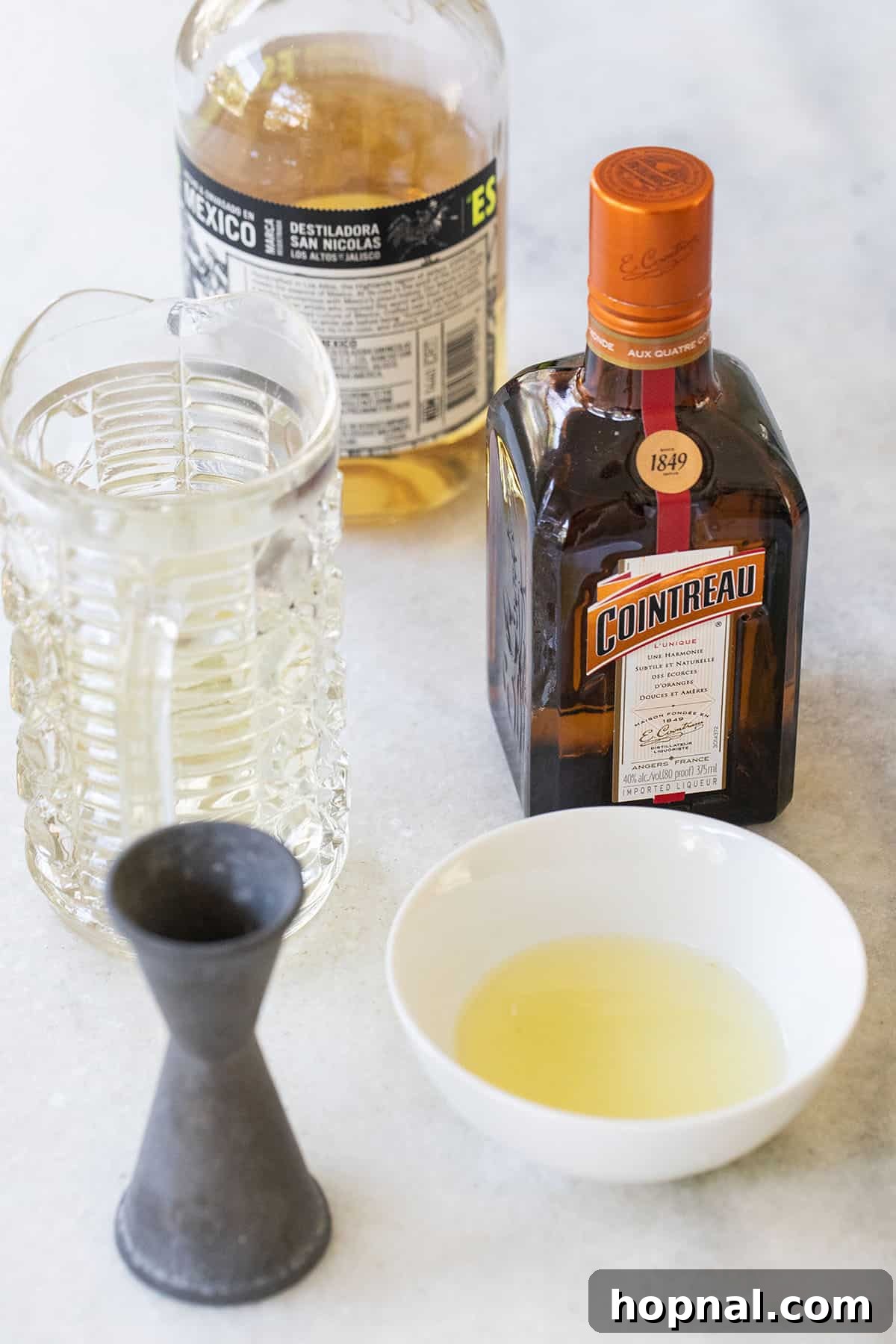 Zesty Lemon Margaritas 3 High-quality tequila, fresh lemons, Cointreau, and simple syrup laid out on a table, ready for mixing a delicious margarita.
