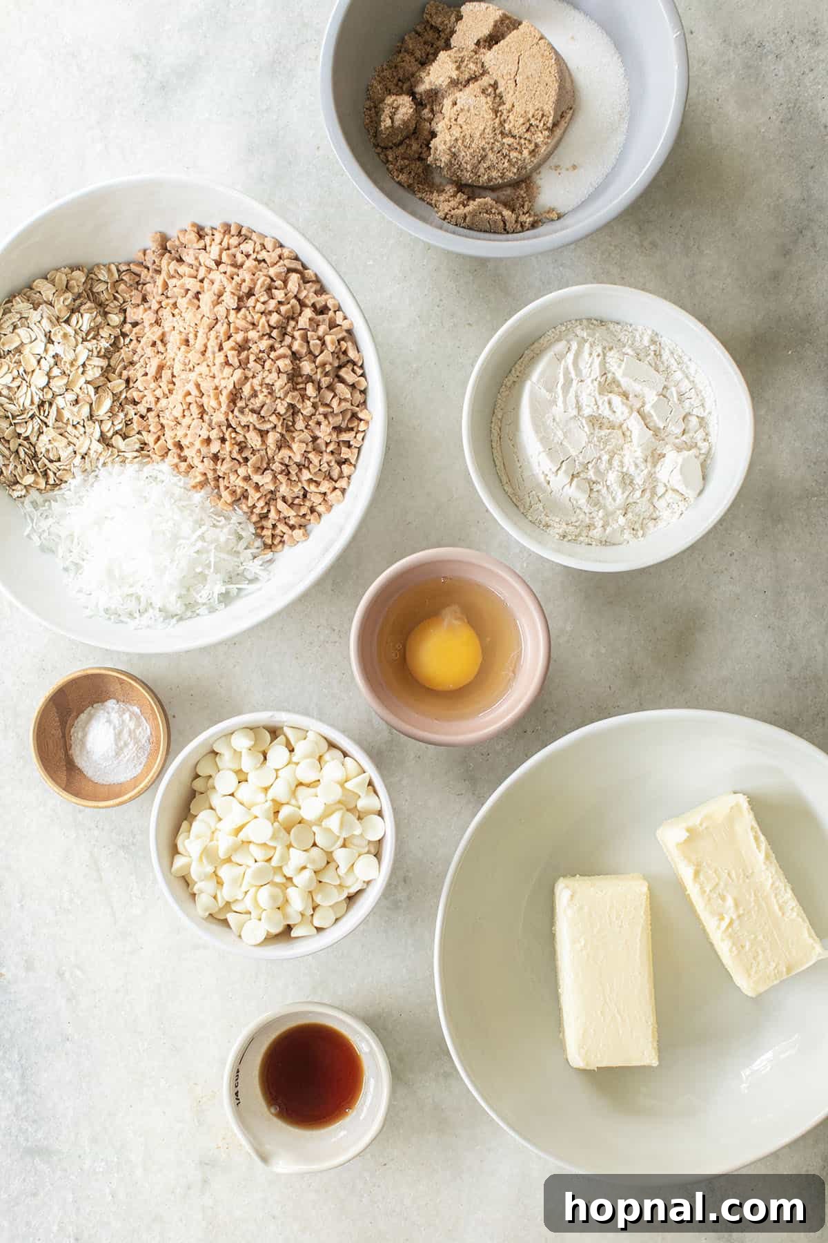Ultimate Kitchen Sink Cookies 3 A selection of fresh ingredients neatly arranged, ready to be used for making kitchen sink cookies, including flour, butter, sugars, and various mix-ins like chocolate chips, toffee bits, coconut, and oats.