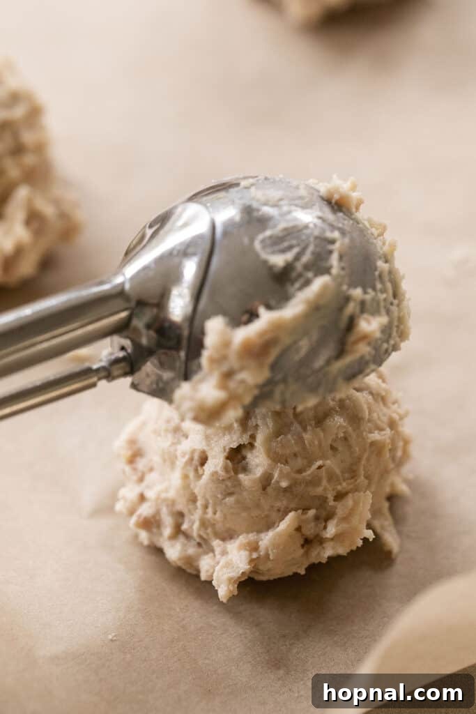 Ultimate Kitchen Sink Cookies 5 A hand using a cookie scooper to portion out kitchen sink cookie dough onto a parchment-lined baking sheet.