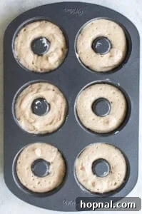 Piping apple cider donut batter into a greased donut pan.