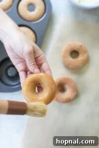 A baked donut being carefully brushed with melted butter.