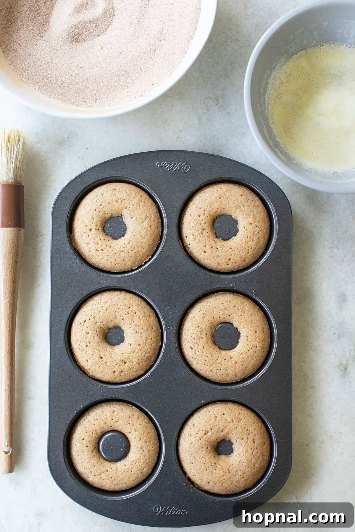 Freshly baked apple cider donuts cooling in a donut pan, showcasing their perfect round shapes and golden color.