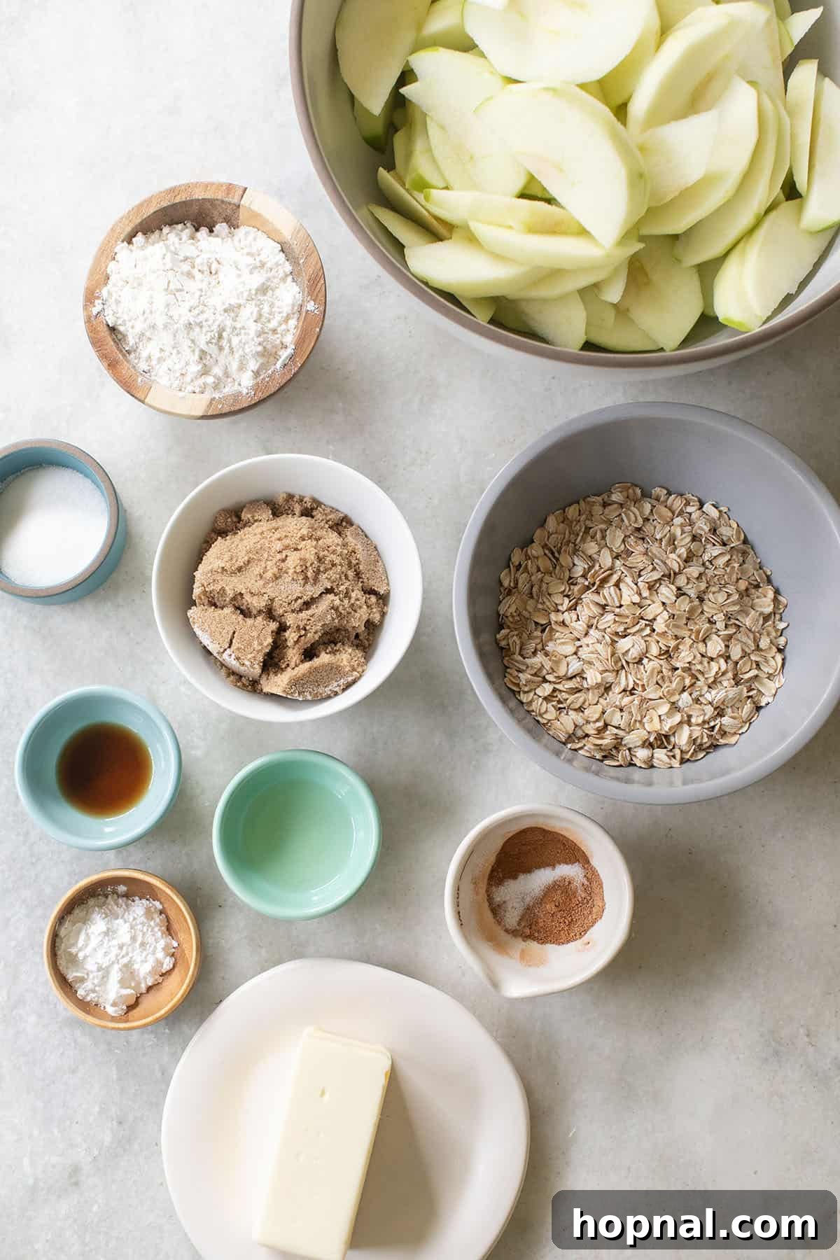 A collection of fresh ingredients laid out for making apple crisp, including apples, oats, flour, sugar, and spices.