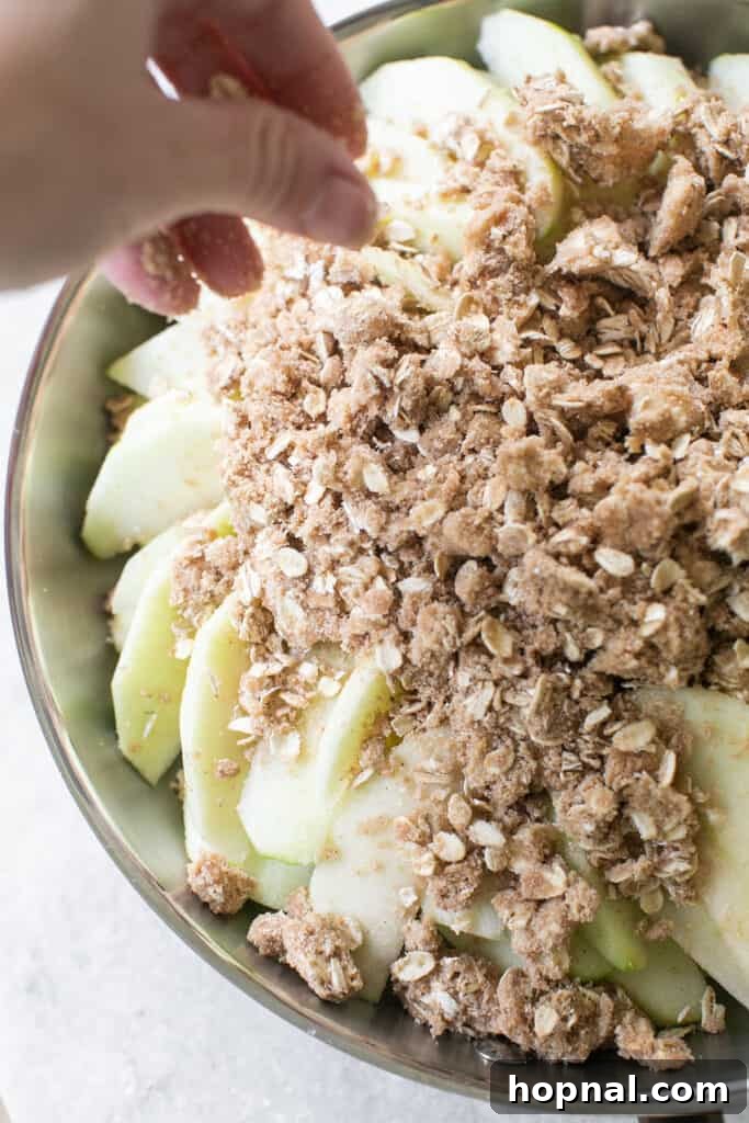 The buttery oat crumble topping generously sprinkled over the layered apples in a baking dish.