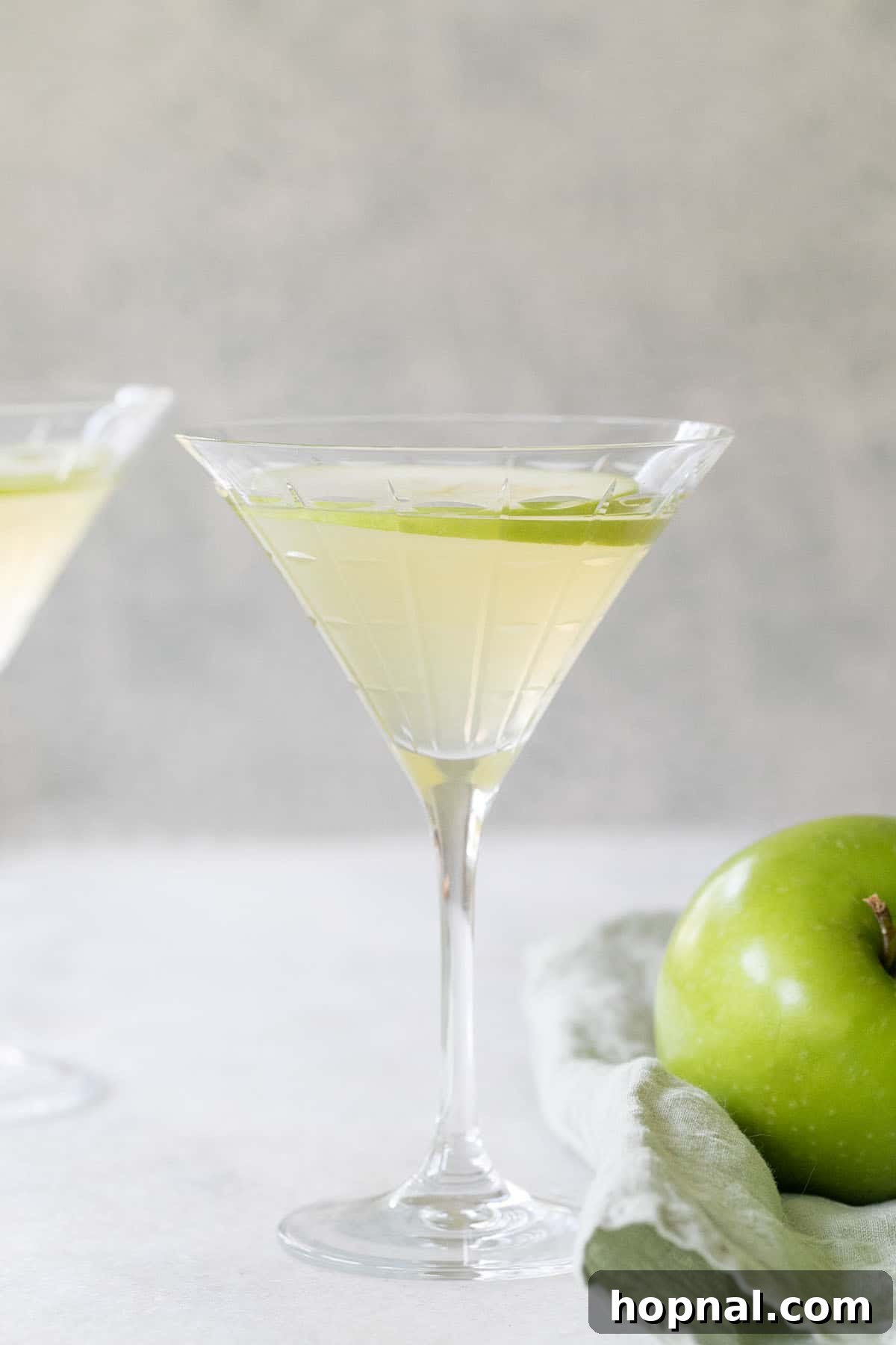 A vibrant green Apple Martini garnished with a thin apple slice, reflecting the crisp, juicy apple flavor of the cocktail.