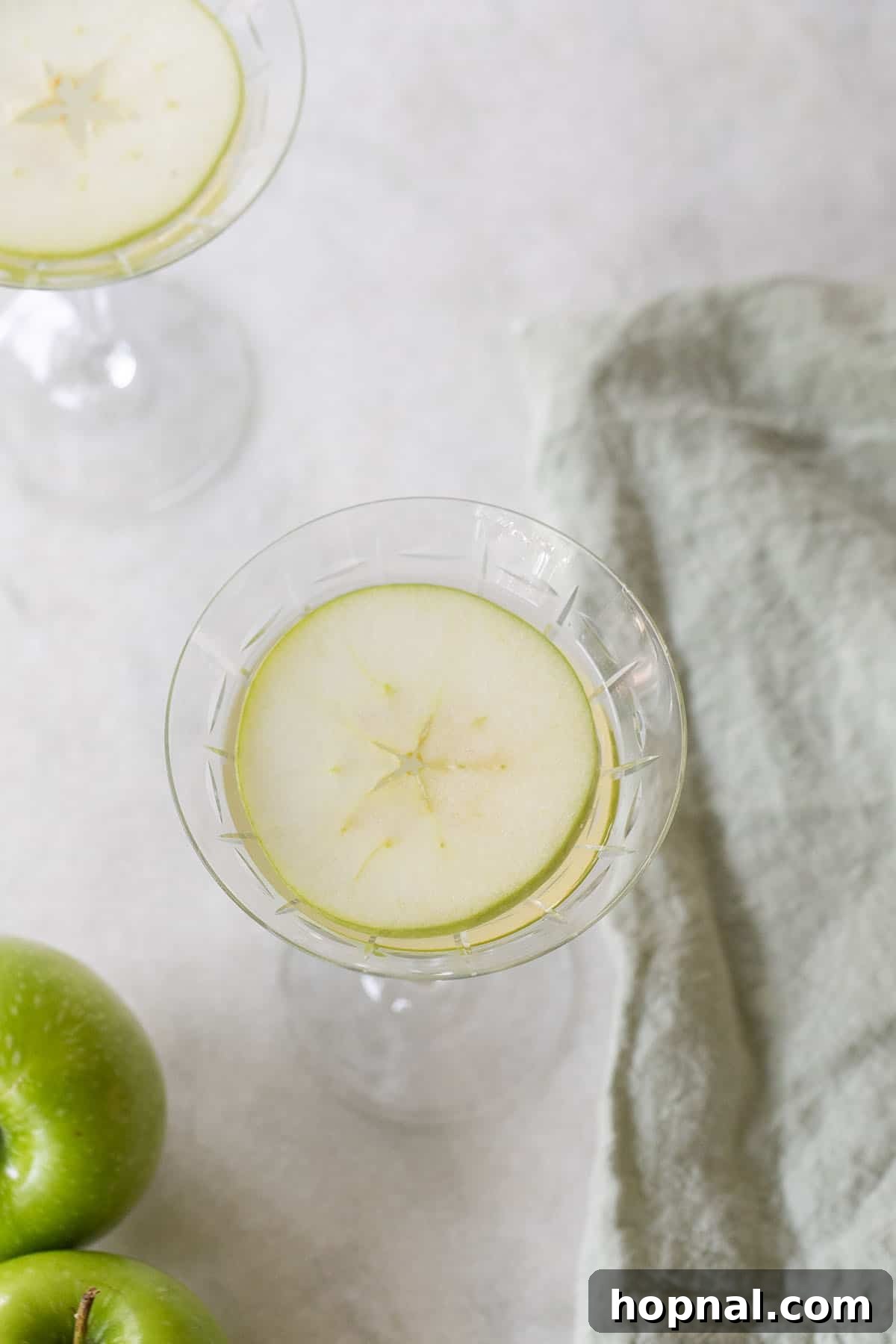 A beautifully presented Appletini garnished with two thin slices of fresh apple, emphasizing its crisp, natural apple flavor and inviting presentation.