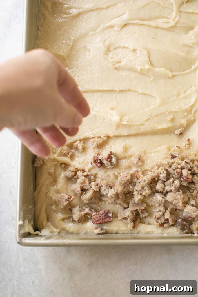 Generously adding crumb cake topping over the smooth cake batter in a pan.