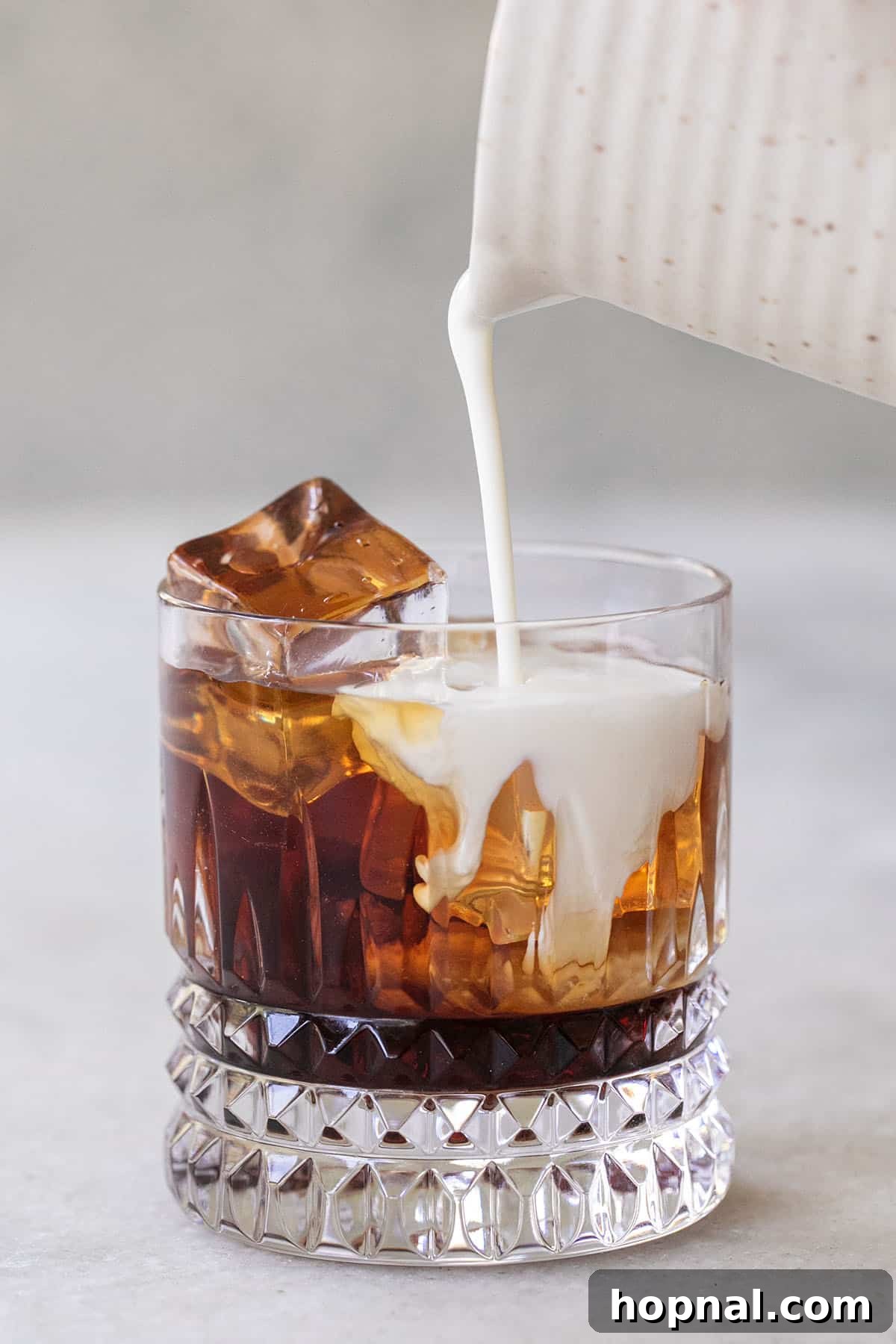 Cloud White Russian 5 Cream being poured over Kahlúa and vodka in a glass, creating a layered effect
