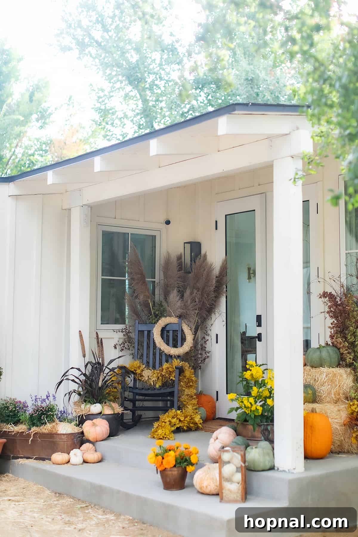 A charming front porch decorated for fall with pumpkins, flowers, and wreaths. A beautifully arranged front porch showcasing an inviting fall decor with an assortment of pumpkins, vibrant autumn flowers, and welcoming wreaths.