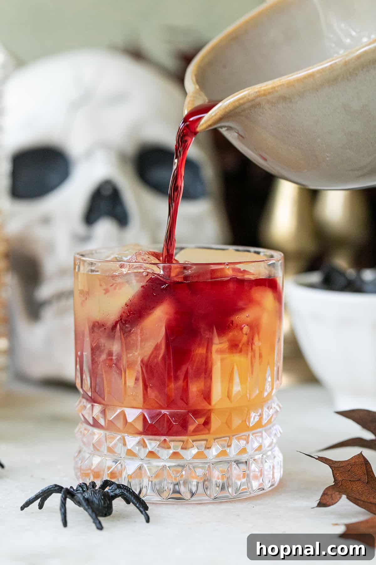 Pomegranate juice being slowly poured over a Witches Brew cocktail, creating a mesmerizing, spooky swirl effect.