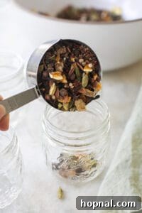Scooping mulled wine spices into a glass jar for storage or gifting.