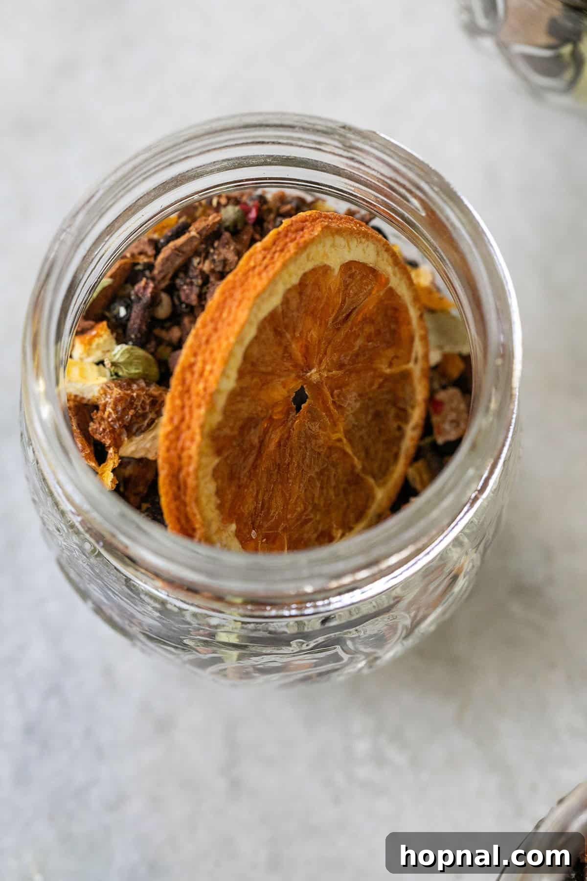 Dried spices elegantly arranged in a glass jar with an orange peel, emphasizing their aesthetic and aromatic appeal.
