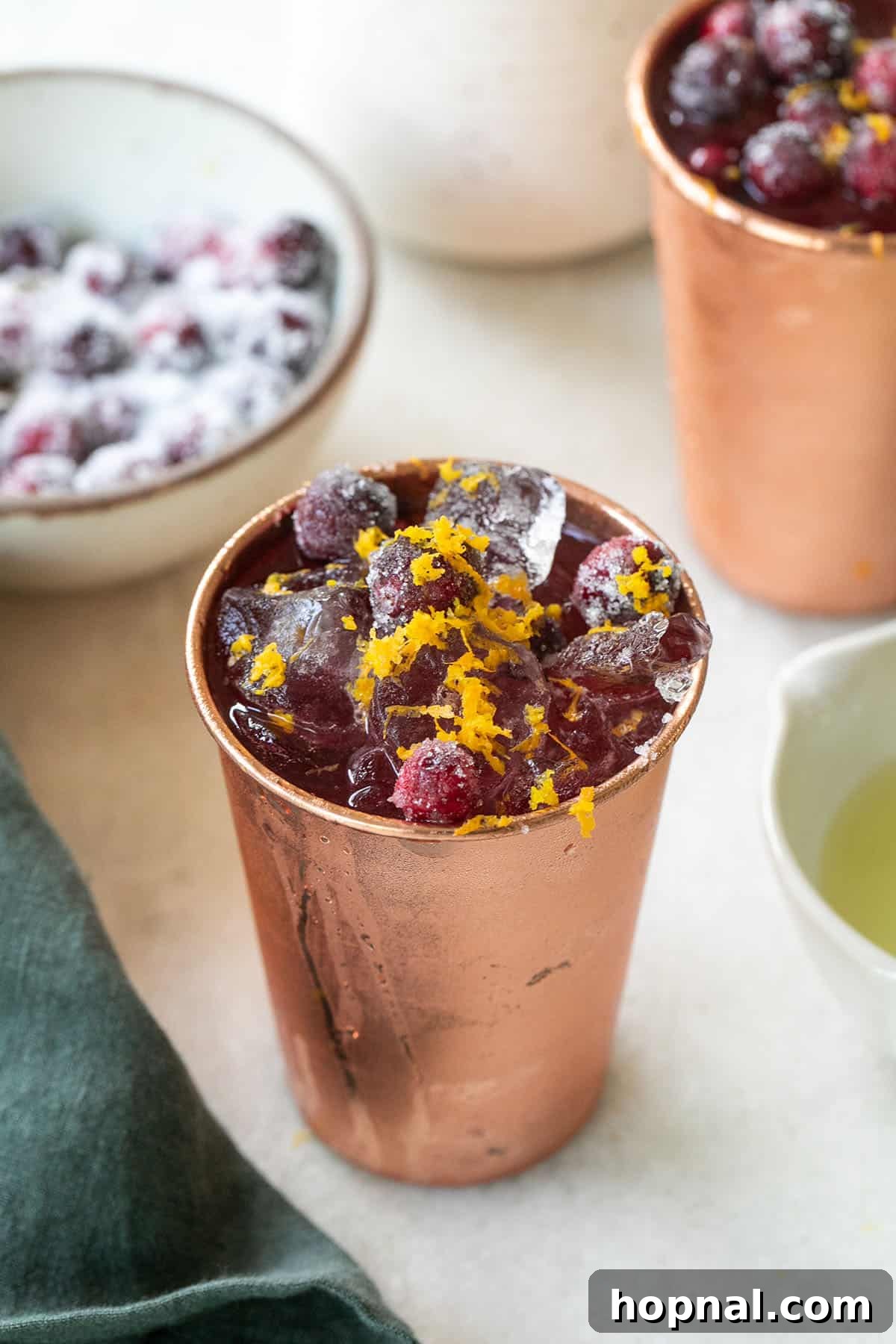 Spiced Cranberry Mule 2 cranberry Moscow mule in a copper cup with orange zest and sugared cranberries.