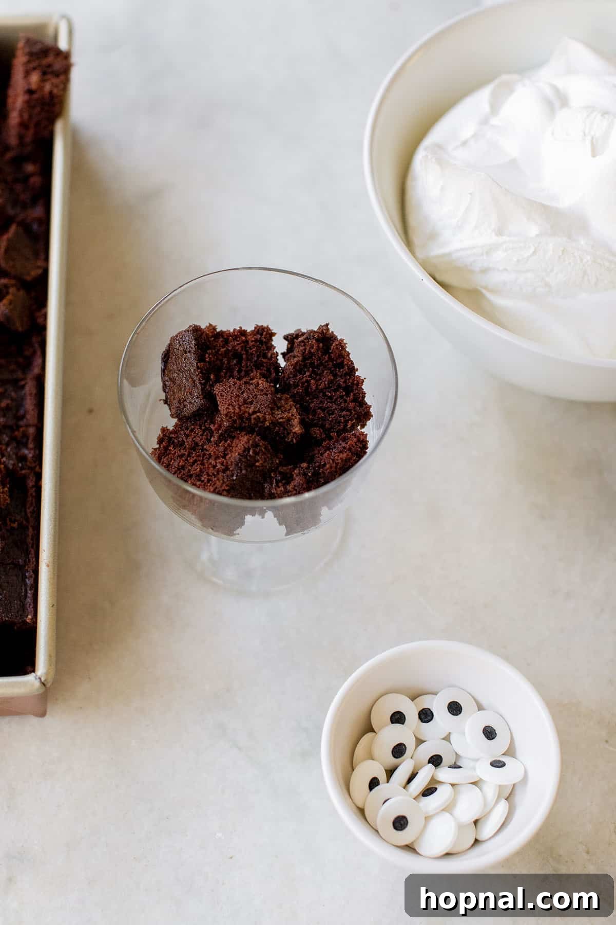 The initial layer of chocolate cake cubes carefully placed at the bottom of a clear mini trifle dish, the first step in assembling an easy Halloween dessert
