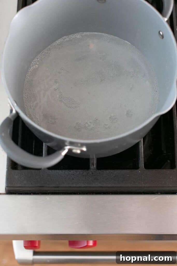 Granulated sugar and water gently boiling in a saucepan, forming a light caramel base for the eggnog.