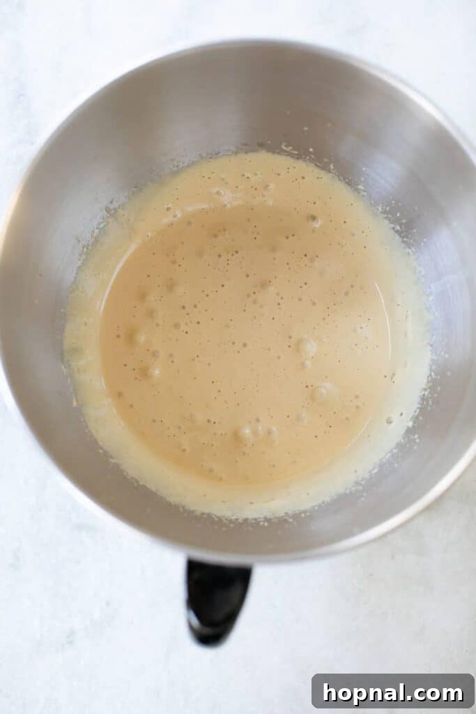 A close-up of egg yolks being vigorously whisked with brown sugar and vanilla until thick and creamy.