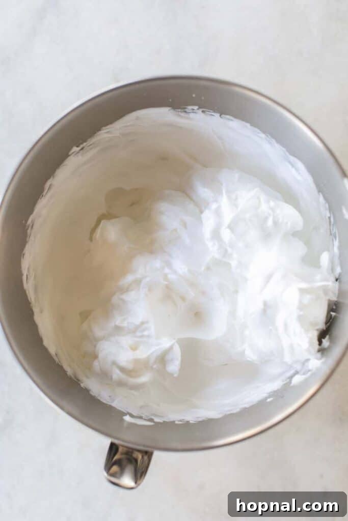 Stiff, glossy peaks of whipped egg whites in a mixing bowl, ready to be incorporated.