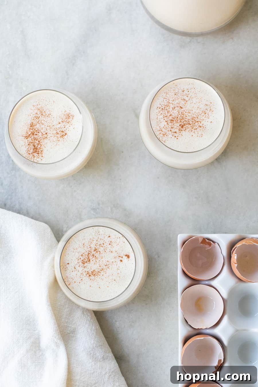 A festive spiked eggnog Christmas cocktail in a clear glass, beautifully garnished with a sprinkle of cinnamon on top.