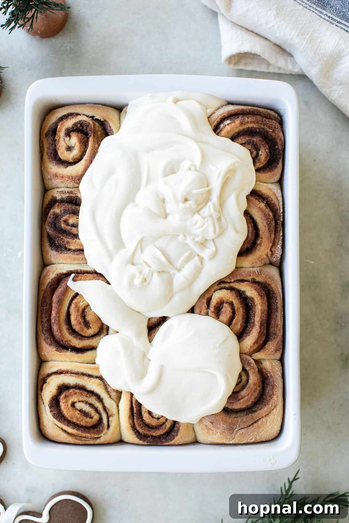 Festive Eggnog Cinnamon Buns 6 Baked eggnog cinnamon rolls being drizzled with generous amounts of eggnog icing.