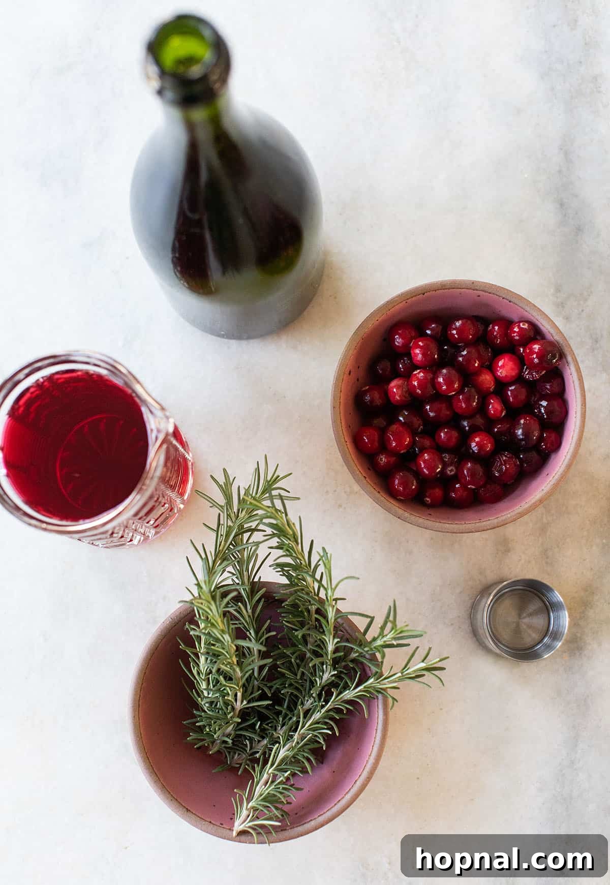 Ingredients in a poinsettia drink on a table: cranberries, rosemary and juice.