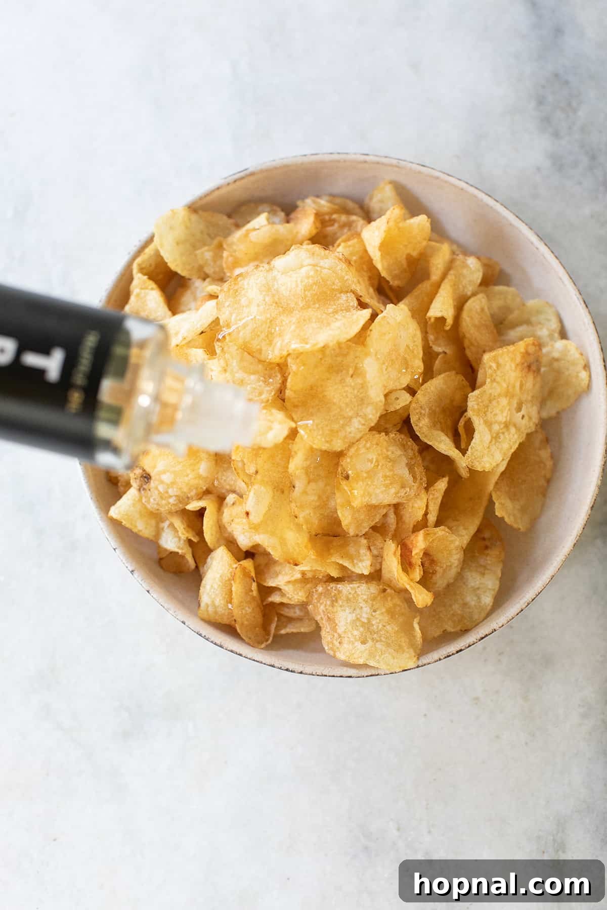 Expertly pouring rich truffle oil over a generous bed of crispy potato chips, preparing them for the prosciutto topping.