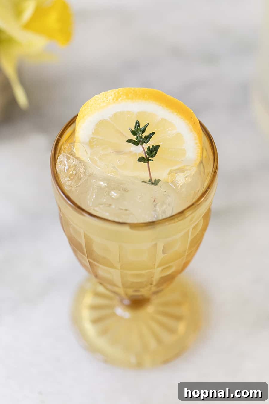 Spiked Tequila Lemonade with fresh thyme garnish in a yellow glass