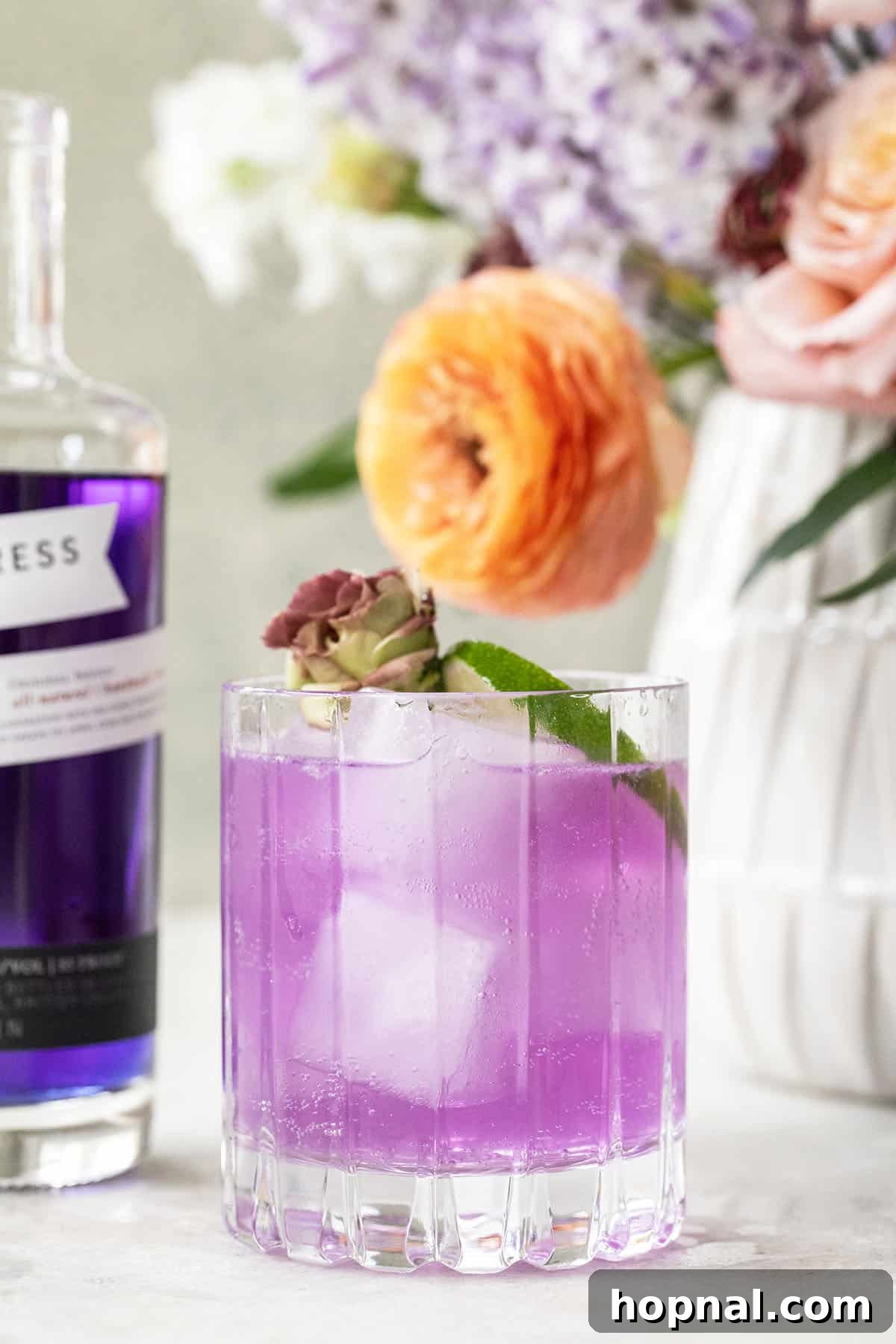 A striking purple cocktail made with Empress gin, garnished with fresh berries and a lime.